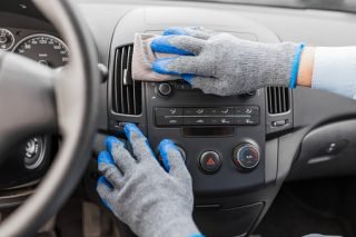 Close up of man hands wearing protective gloves and cleaning car interior dashboard with microfiber cloth. Cleaning salon concept.